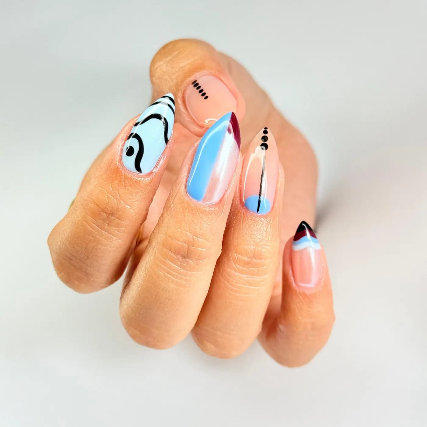 Nail art abstracto em azul-claro, rosa e preto, com traços desenhados à mão sobre base natural