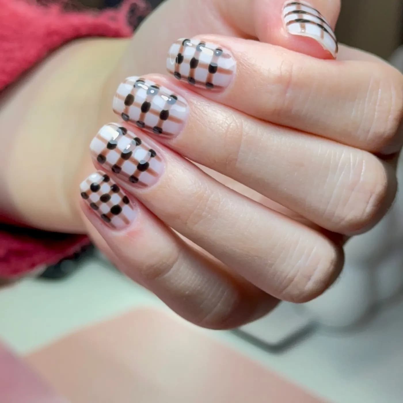Unhas curtas com padrão xadrez preto e branco e pérolas na base